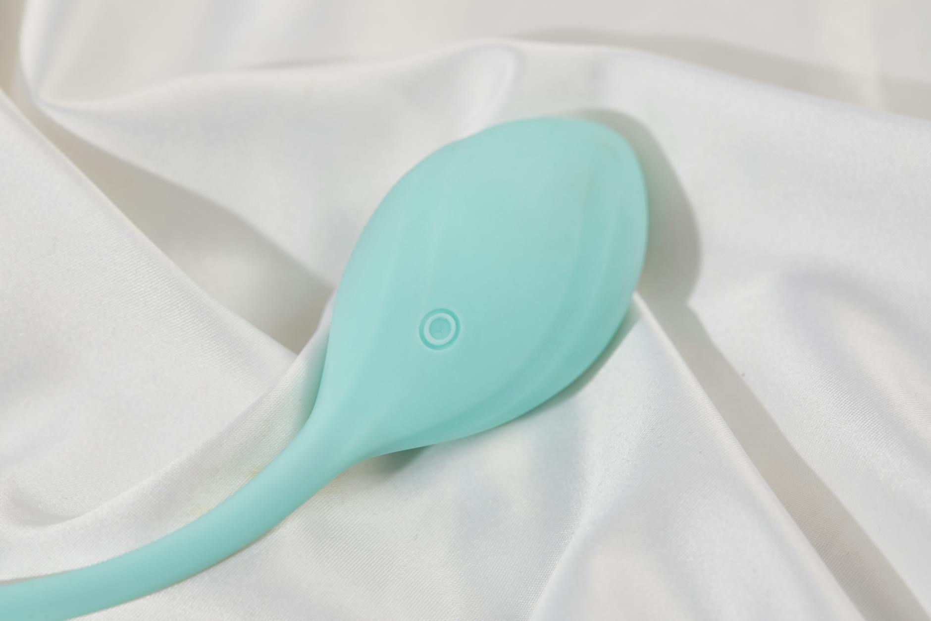 A sleek teal lemon vibrator on white silk fabric, symbolizing intimacy and pleasure