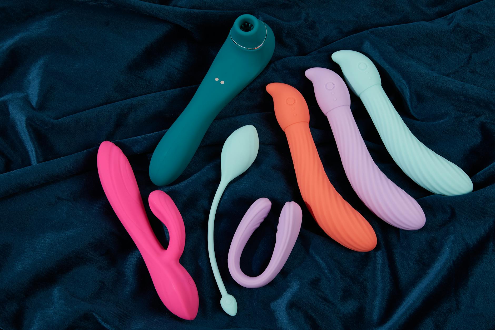 Frau mit Brille hält einen blauen und einen rosa Silikon-Vibrator in nachdenklicher Pose