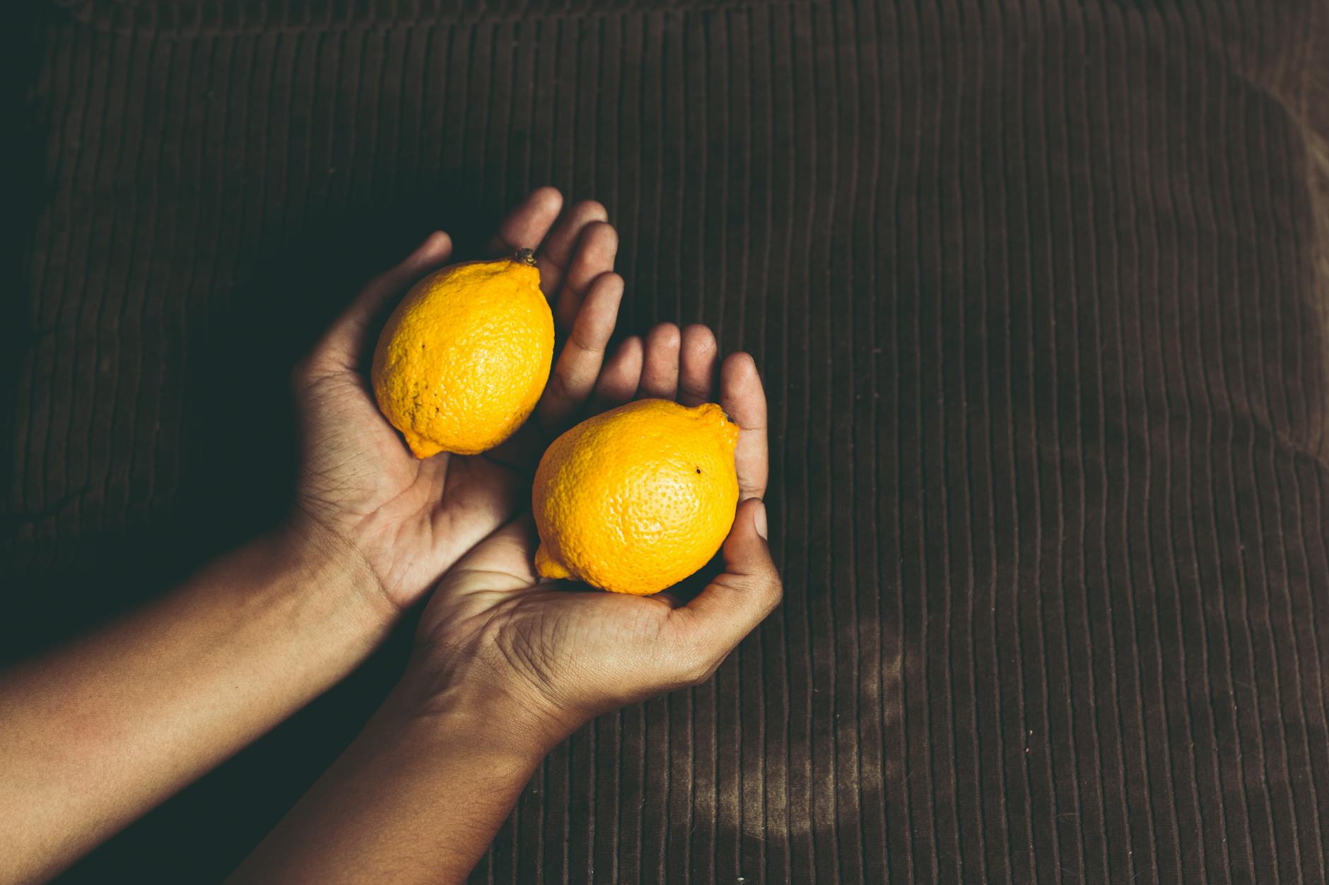 Close-up of two fresh lemons held in cupped hands, symbolizing patience and natural timing in pleasure