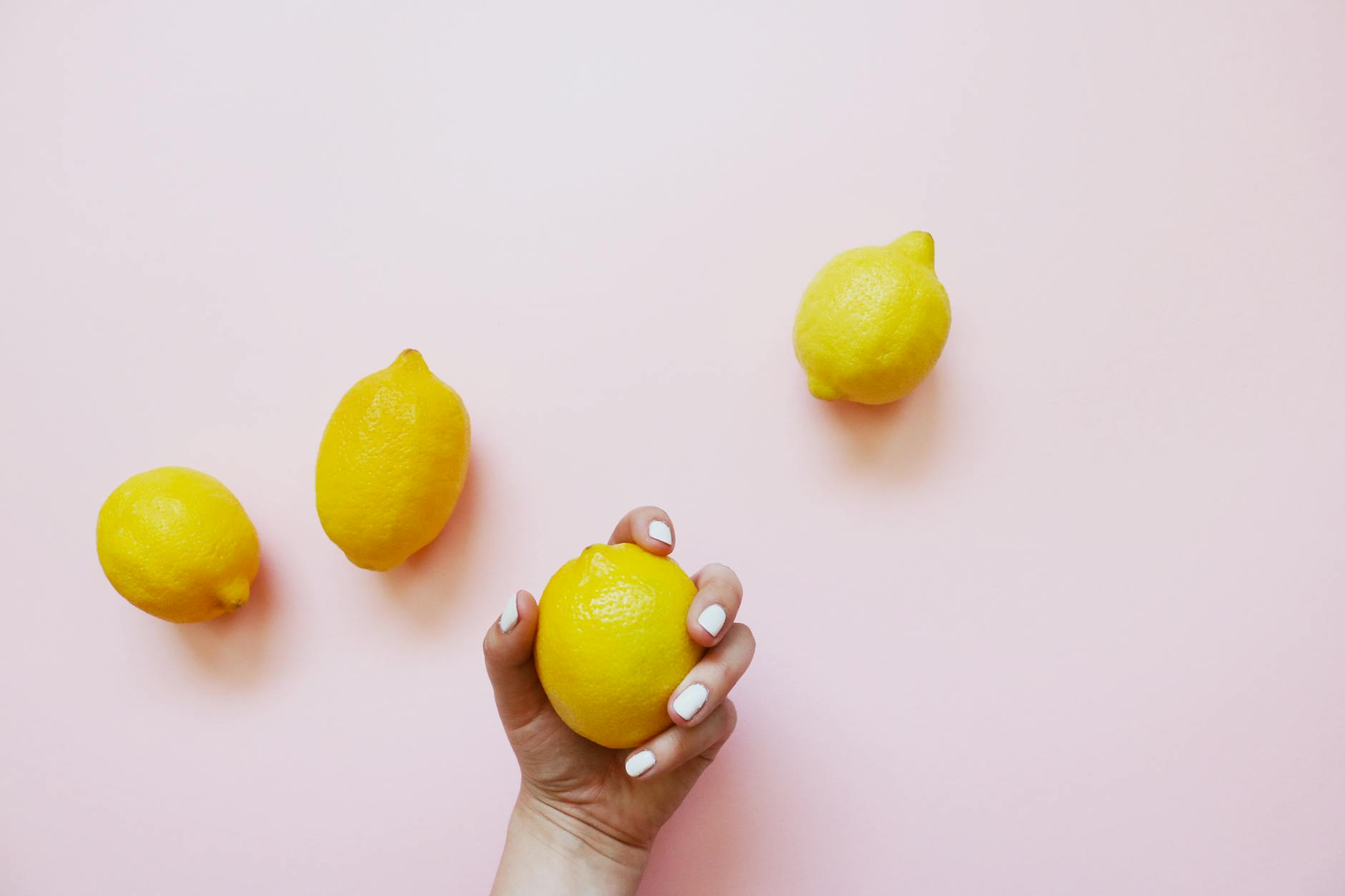 A hand holding a fresh lemon on a soft pink background, symbolizing calm and focus