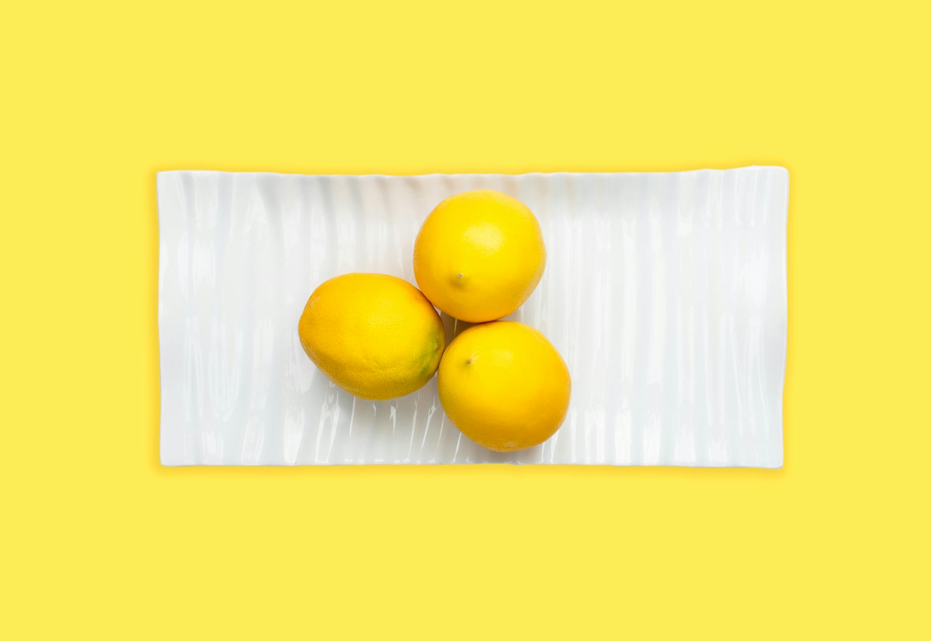 Fresh lemons arranged on a white plate with a vibrant yellow background, symbolizing openness and freshness in intimate conversations