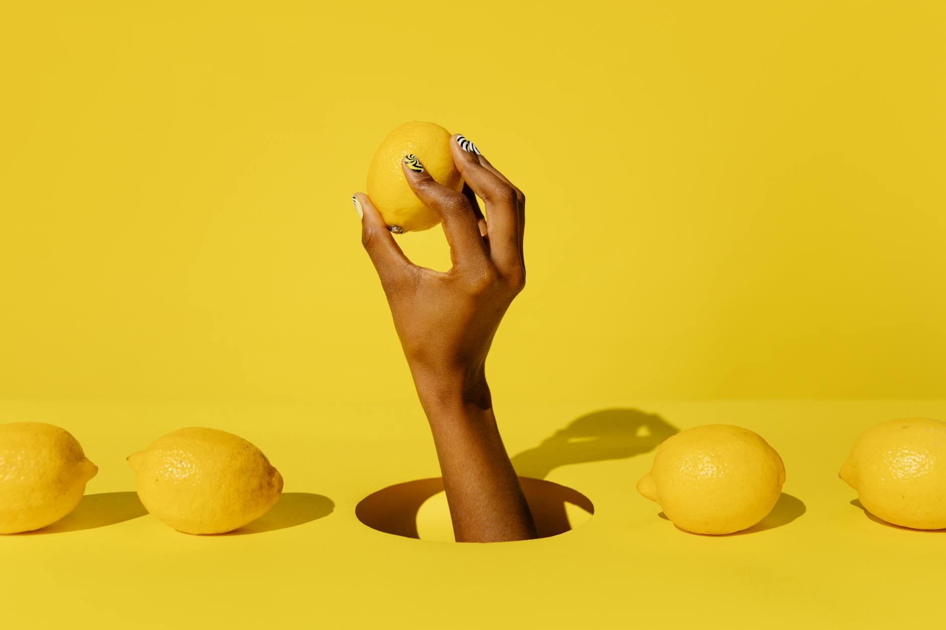 A hand holding a lemon against a vivid yellow background