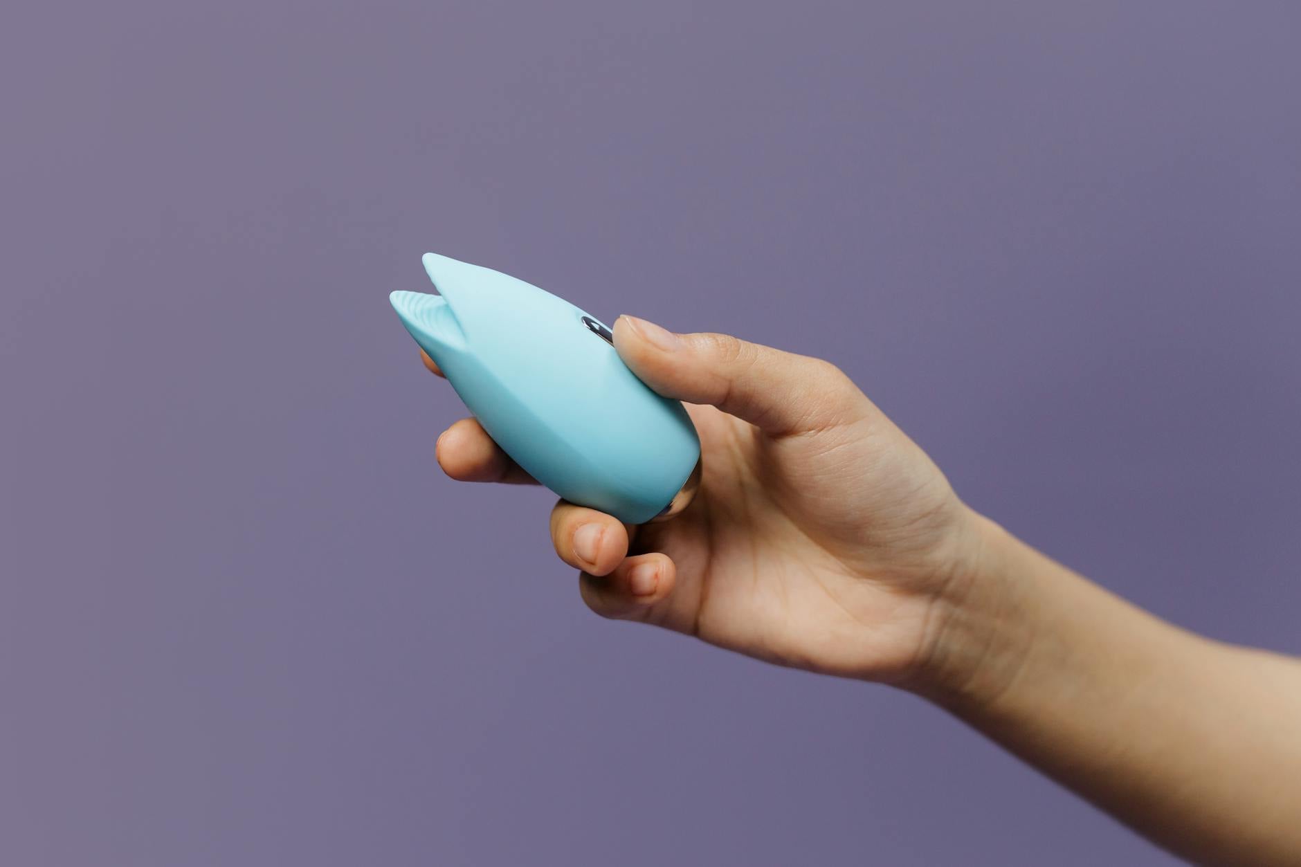 Two hands holding vibrators against a pastel background, representing shared pleasure and partnership