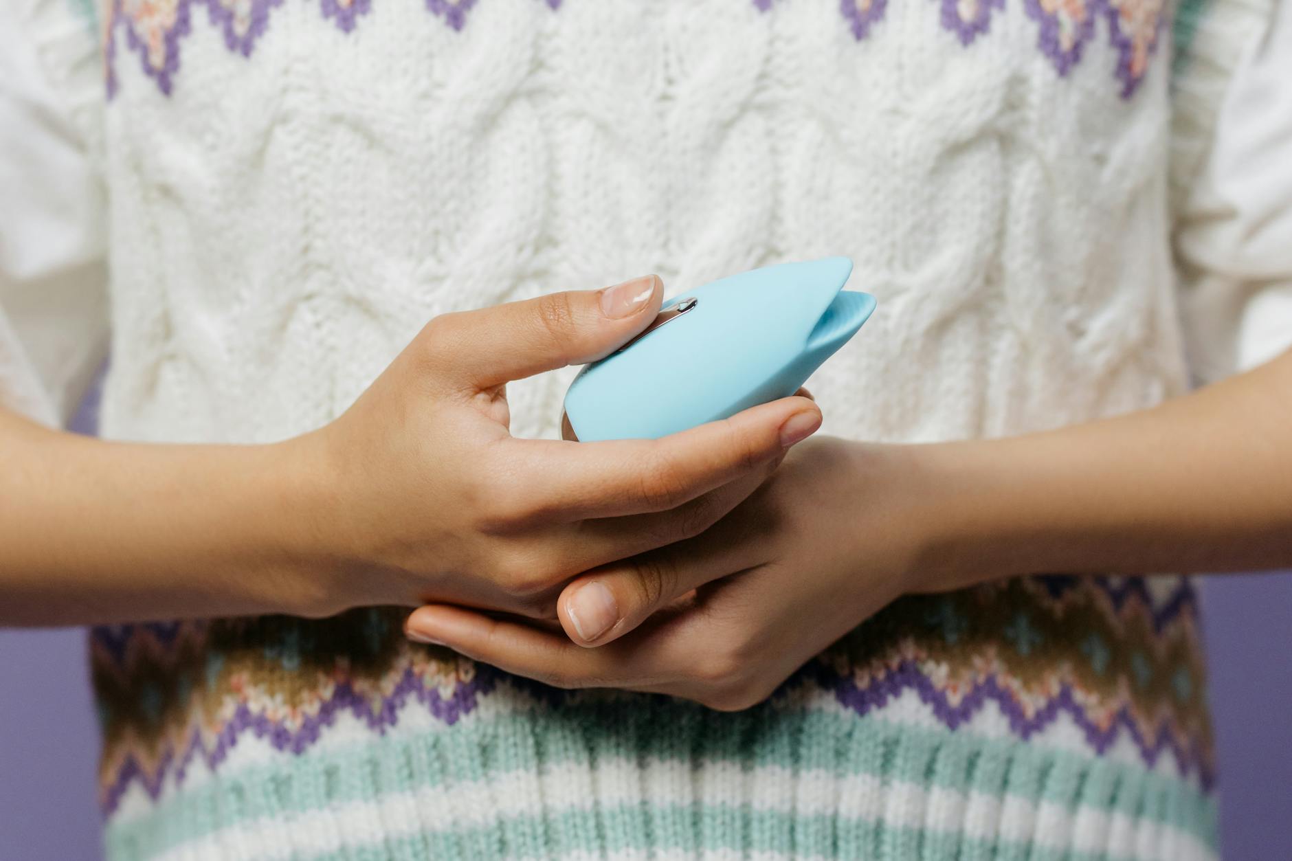 Close-up of hands holding a blue personal massager against a knitted sweater.