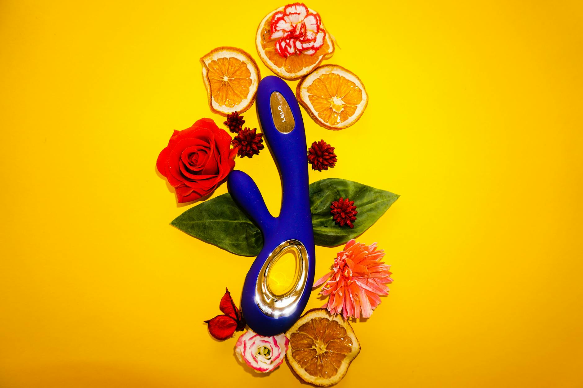 Blue Lemon vibrator surrounded by fresh citrus and flowers on a bright yellow background.